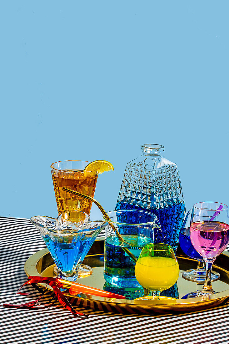 Different varieties of cocktails comprising blue margarita Long Iceland iced tea wine daiquiri in attractive glasses and jar placed on plate on striped cloth against blue background