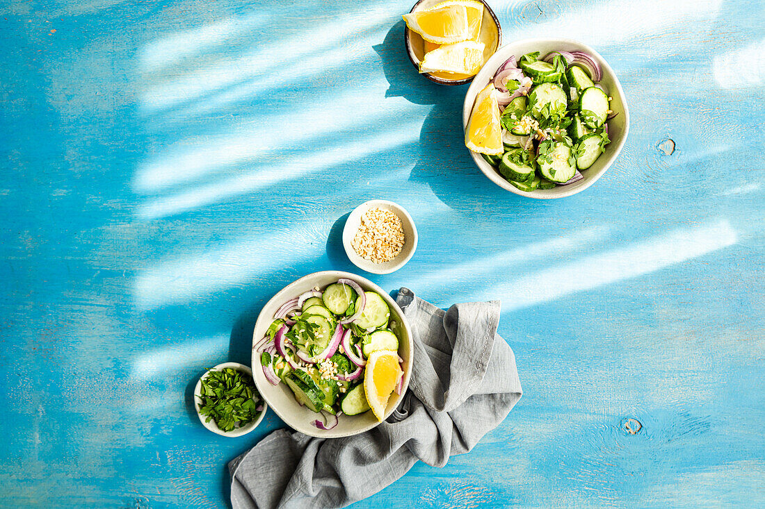 Gesunder Gemüsesalat mit Bio-Gurke, roter Zwiebel, Koriander und gehackten Nüssen auf einem blauen Betontisch von oben