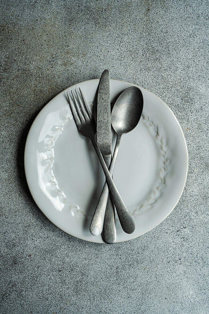 Blick von oben auf Vintage-Besteck auf weißem Teller gegen graue Oberfläche in hellen Küche platziert