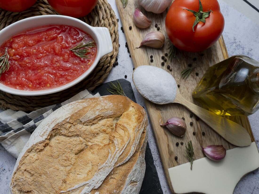 Draufsicht auf eine Schüssel mit Tomatenaufstrich und Vollkornbrot auf dem Tisch vor einer Flasche mit Olivenöl, Knoblauch und einem Löffel mit Salz