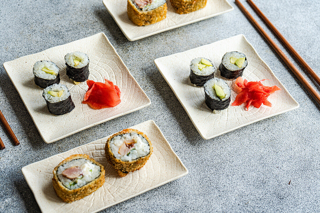 Various sushi rolls placed on plates with chopsticks and soy sauce on white background
