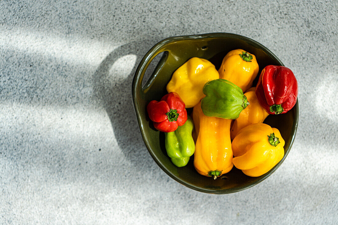 Top view of different colored peppers placed in a round black ceramic bowl on a concrete background