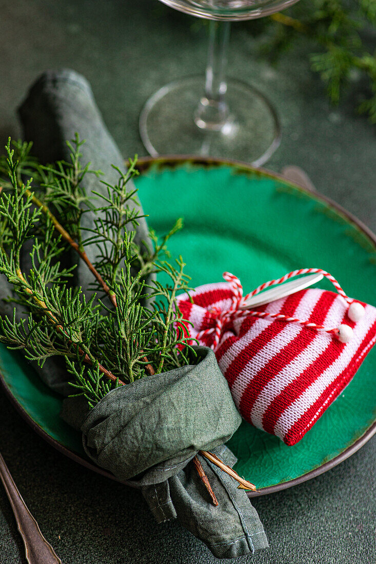 Little Christmas bag and fir sprigs wrapped in handkerchief on plate placed on green table near glass and forks