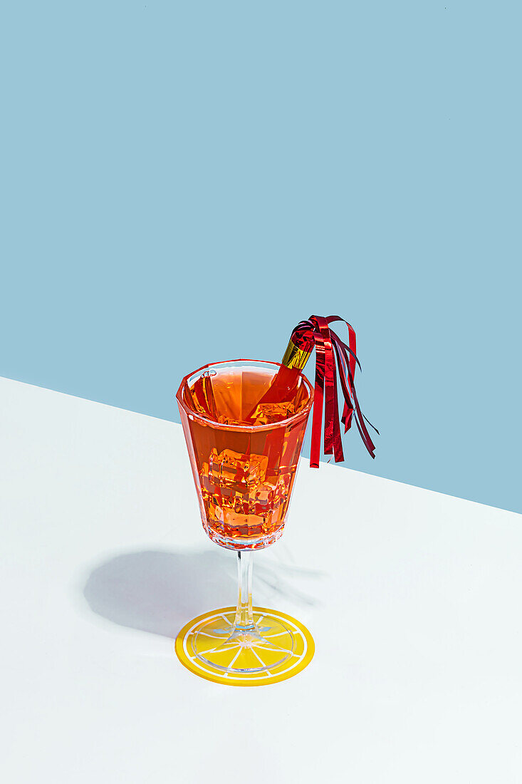 A decorative vintage glass with a vibrant red ribbon against a minimalist blue and white backdrop, casting a soft shadow.