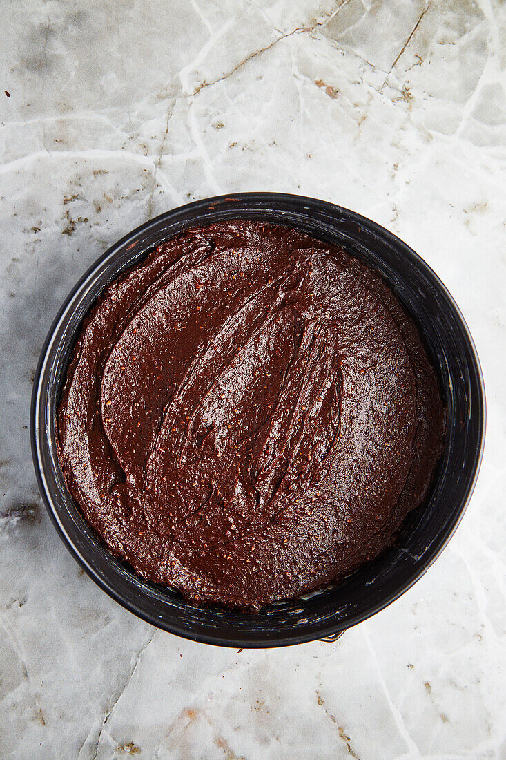 Draufsicht auf eine mit Schokoladenteig gefüllte Backform für Kuchen auf grauem Marmor