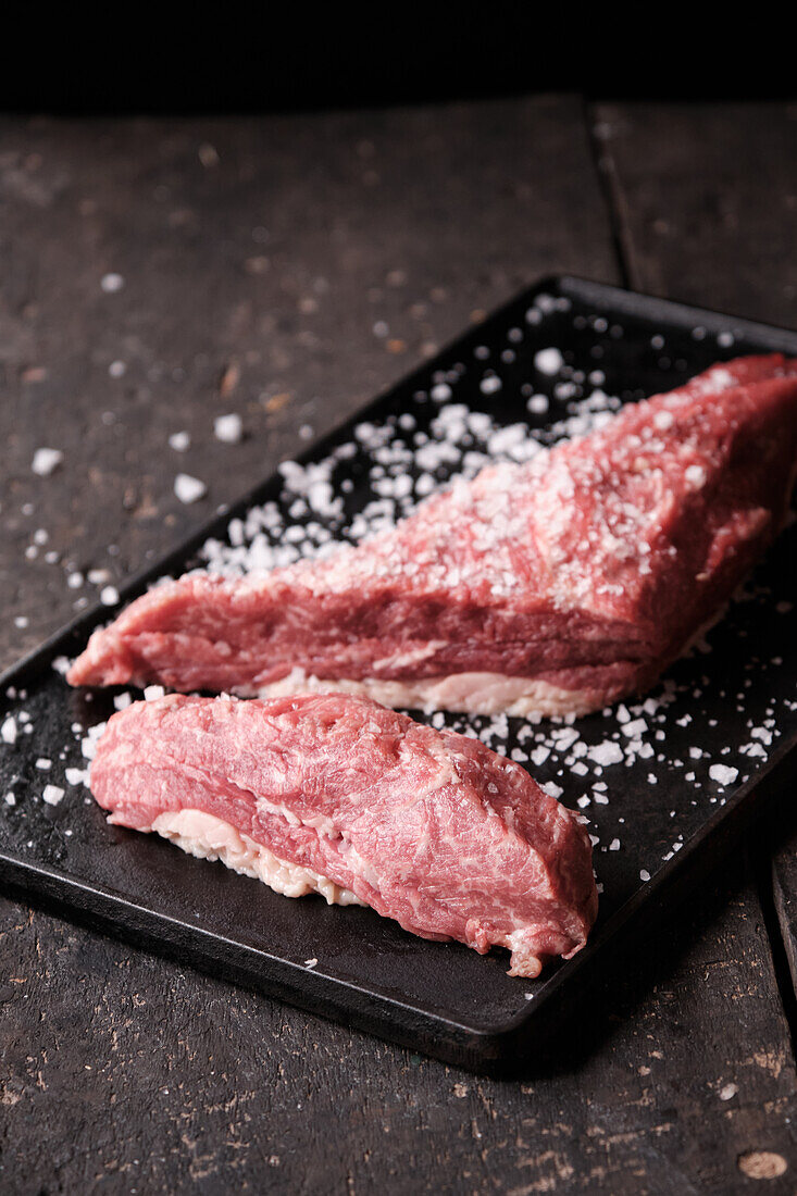 From above of raw meat pieces placed on black tray sprinkled with salt for cooking traditional Ecuadorian dish