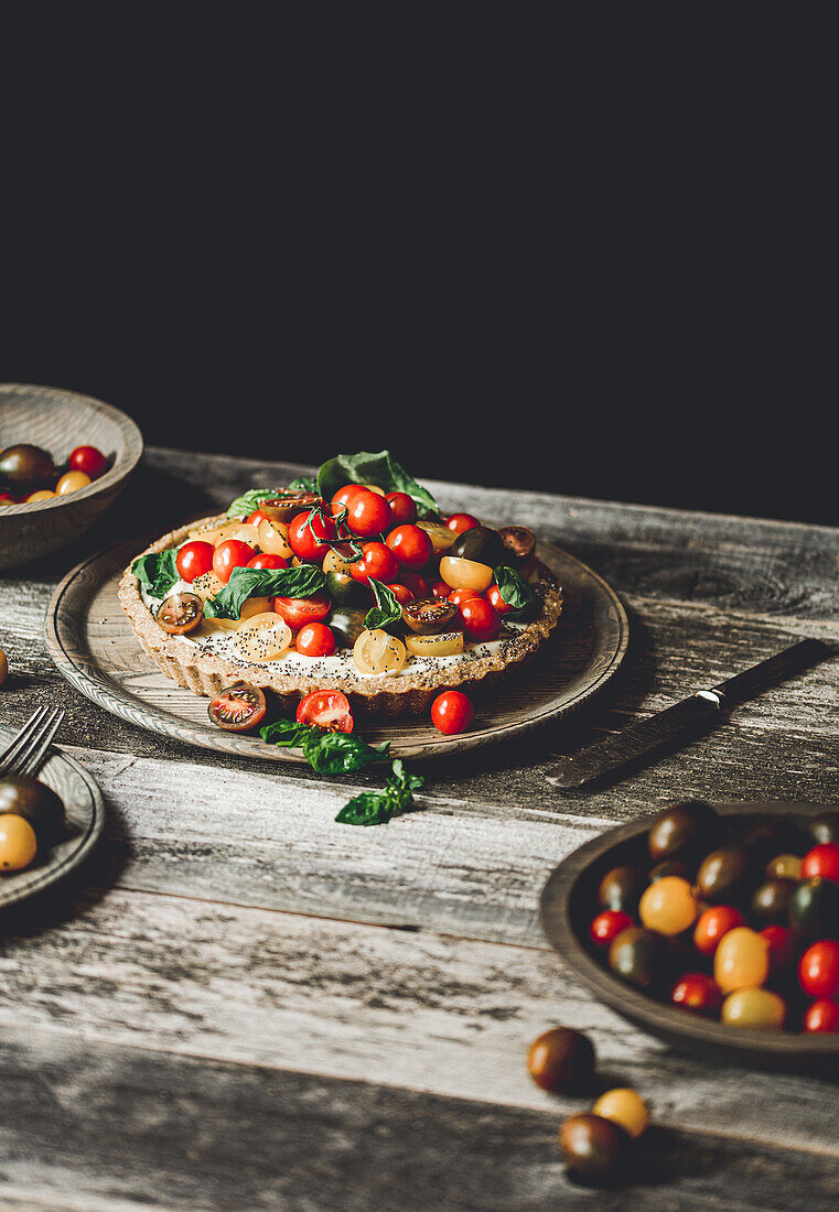 Delicious healthy vegan tart garnished with ripe colorful cherry tomatoes and herbs on plate on rustic wooden table