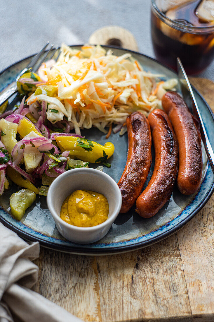 Vegetables and sausages on plate served with glass of cola drink