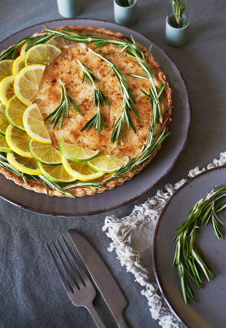 From above of round lemon pie with decorated with lemon slices and rosemary sprigs on table in the kitchen