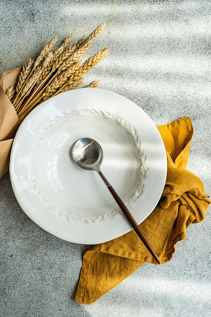 Top view of summer table setting with plate and spoon near napkin and wheat placed on gray table