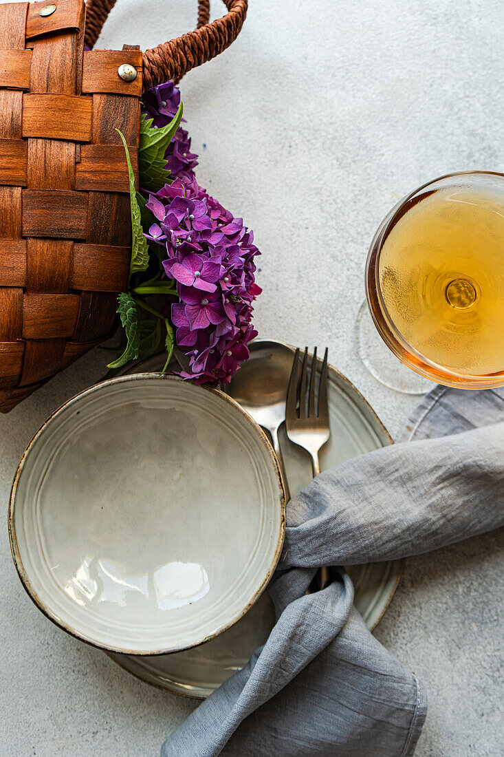 Draufsicht auf eine lila Hortensie, die auf einem weißen Tisch neben Keramiktellern und einem Glas mit Getränk steht