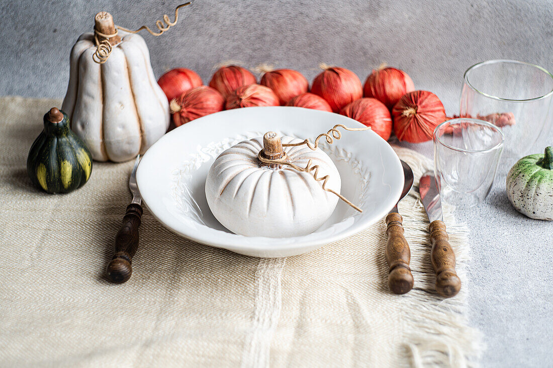 High angle of autumnal table setting with white pumpkin on plate placed on table near cutlery, glasses and red onions