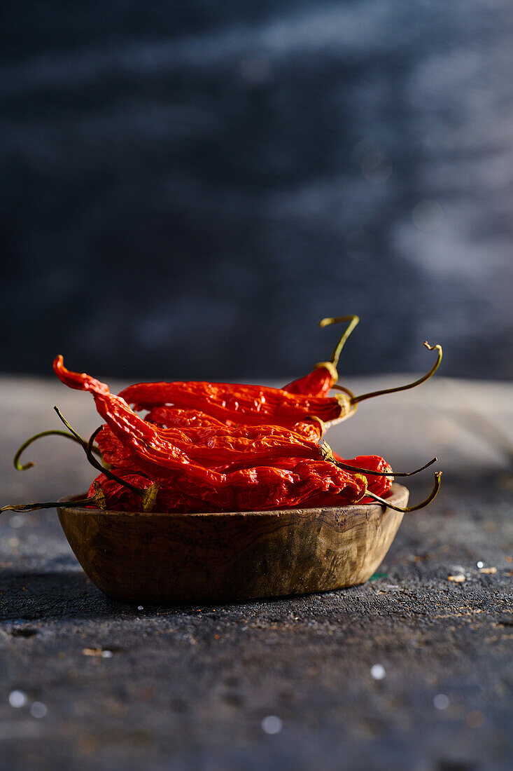 Wooden bowl with dried red hot peppers placed on table against blurred background