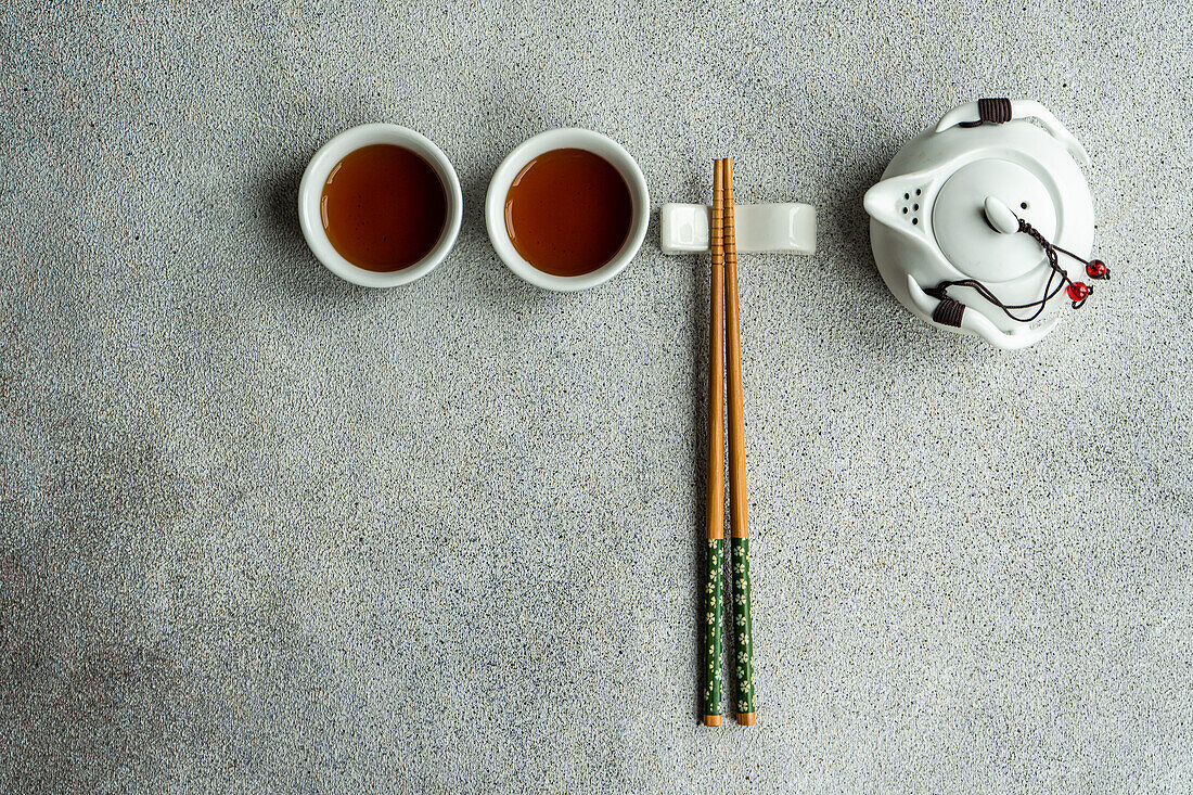 Draufsicht auf Teeservice im asiatischen Stil mit Stäbchen vor grauem Hintergrund