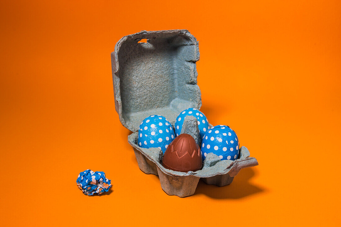 Close-up of some blue easter eggs inside a gray cardboard box on an orange background