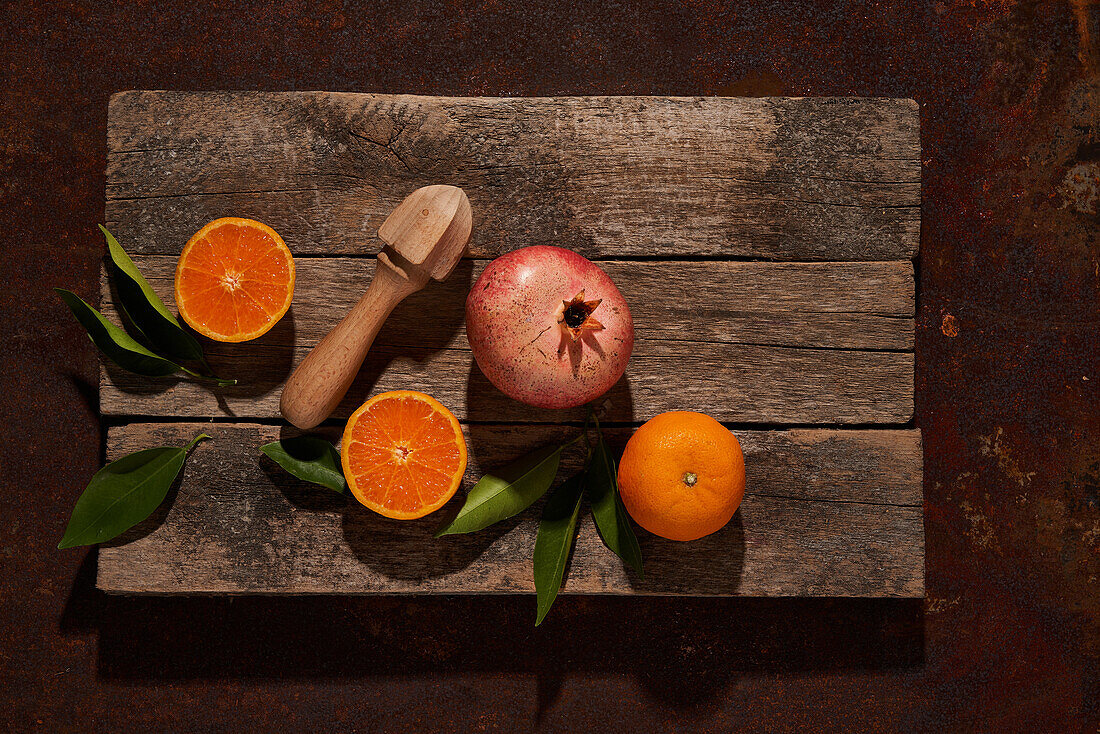 Draufsicht auf eine reife Orange und einen Granatapfel mit einer manuellen Zitruspresse aus Holz vor einem dunkelbraunen Hintergrund