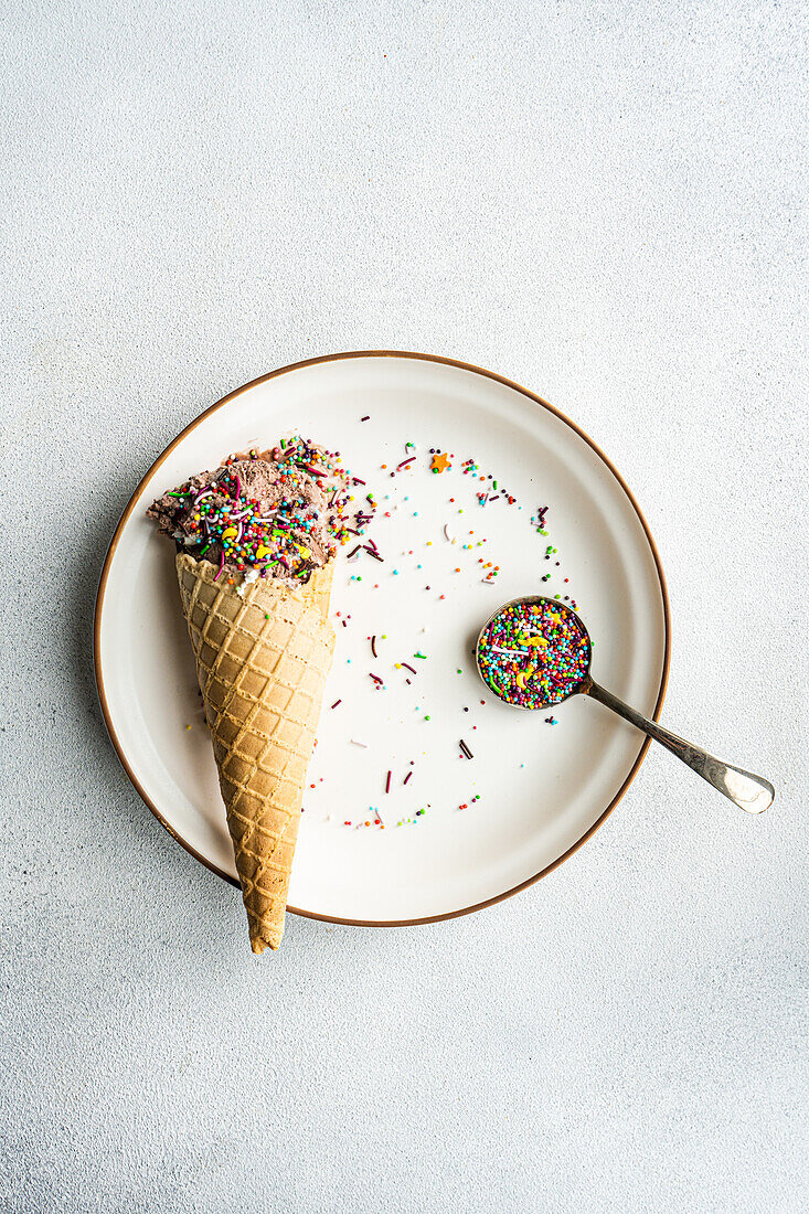Top view of a waffle cone with coffee and chocolate ice cream with a spoonful of multicolored sugar sprinkles on top in a ceramic dish