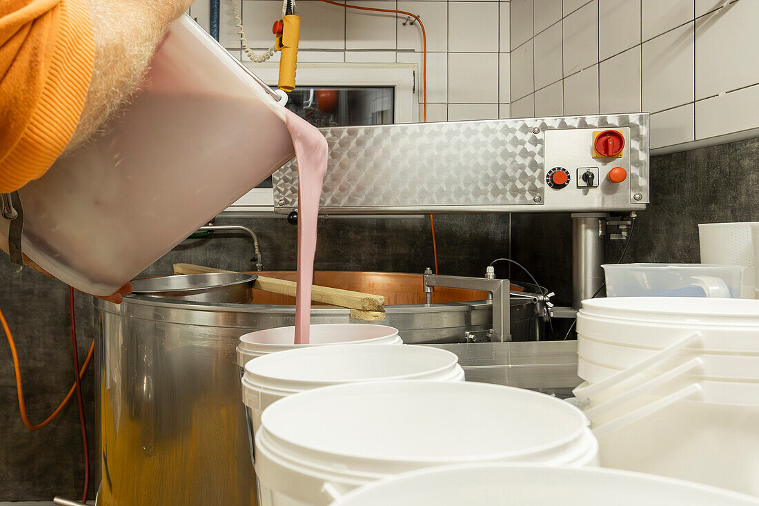 Ein Käser gießt frische, cremige Milch in einen großen Stahltrog, um sie gerinnen zu lassen - der erste Schritt bei der Käseherstellung in einer professionellen Küche
