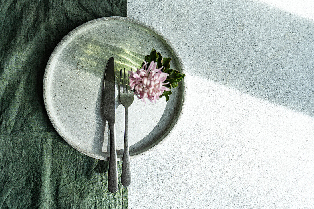 Ein exquisiter gedeckter Tisch mit Besteck und einem kleinen Blumenarrangement auf einem Keramikteller, akzentuiert durch eine strukturierte grüne Serviette