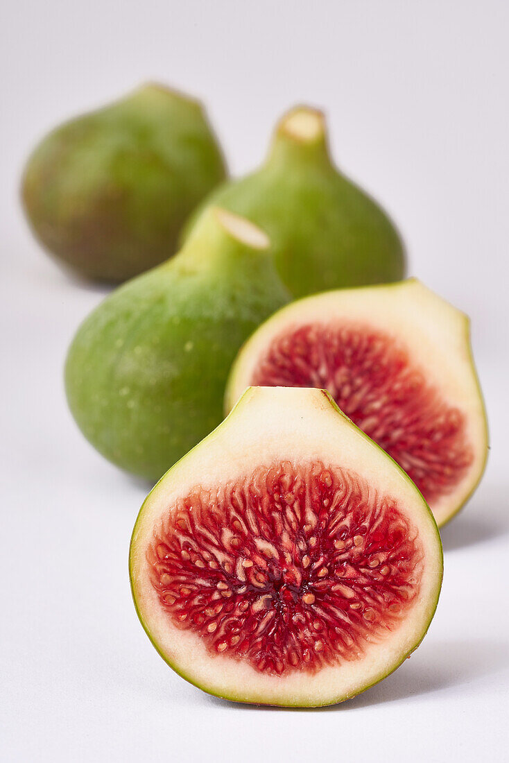 Vibrant fresh figs with one sliced in half, showcasing the red interior against a clean, white backdrop.