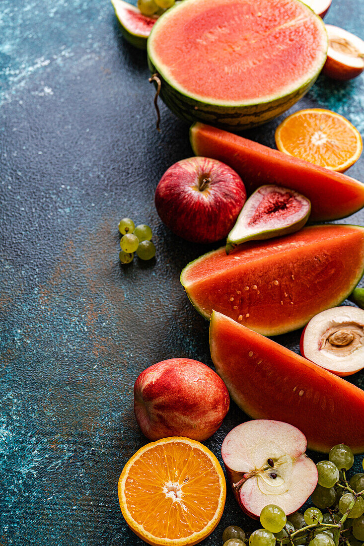 Draufsicht auf einen Rahmen mit Früchten der Saison, bestehend aus Wassermelone, Orange, Weintrauben und Äpfeln, auf einer dunklen Fläche