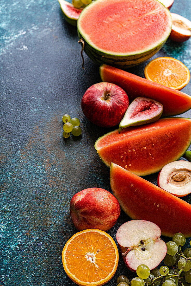 Top view of crop seasonal fruit frame consisting of watermelon, orange, grapes and apples placed on dark surface