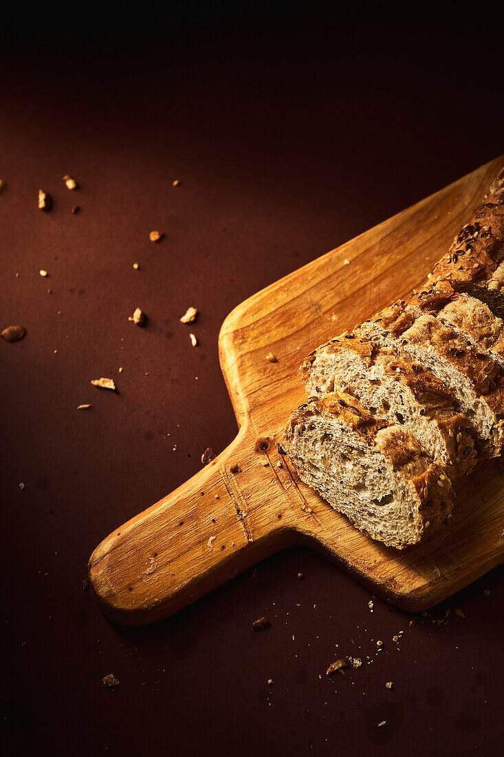 Hoher Blickwinkel auf köstliches, frisch gebackenes Brot mit knuspriger Kruste, bestreut mit einer Mischung aus Samen und auf einem Holzbrett platziert