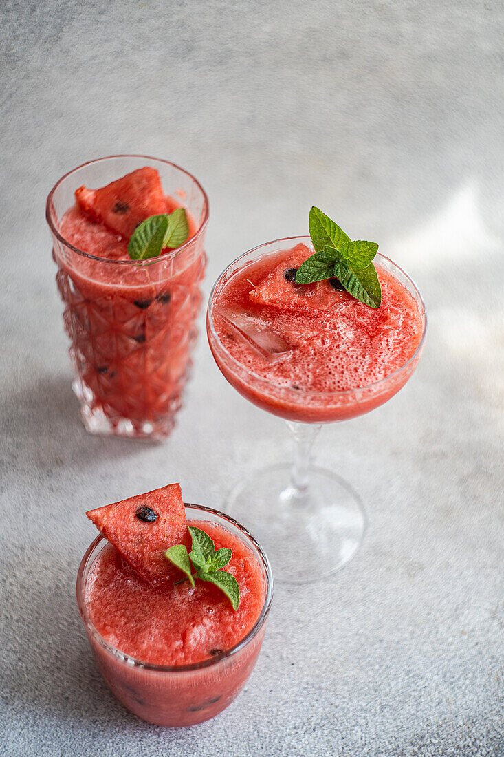 Blick von oben auf Gläser mit Margarita-Cocktail und Wassermelonen-Smoothie, garniert mit Minzblättern, auf grauem Tisch