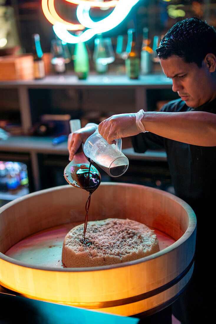 A focused chef is seen mixing sushi rice in a wooden tub called hangiri, essential for the perfect sushi.