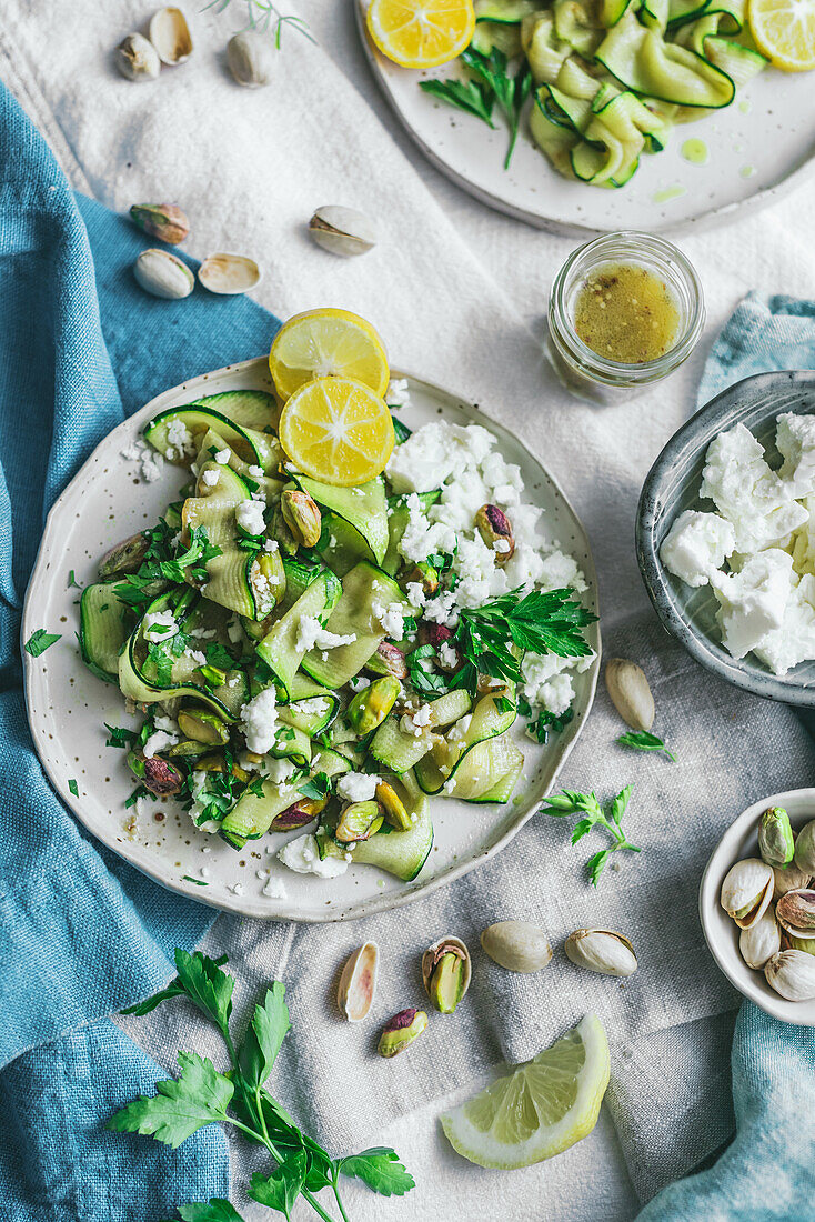 Top view of delicious healthy grilled courgette salad with feta cheese and pistachios served with slices on lemons and herbs on table