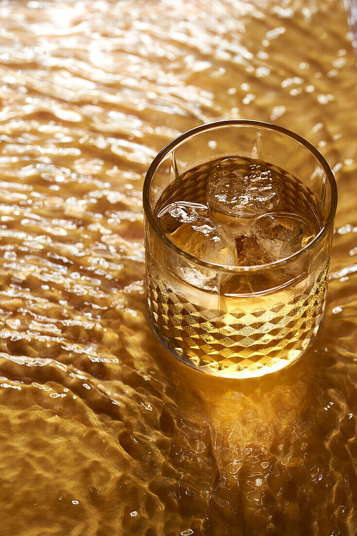 Whiskeyglas mit Eis auf einer strukturierten goldenen Oberfläche