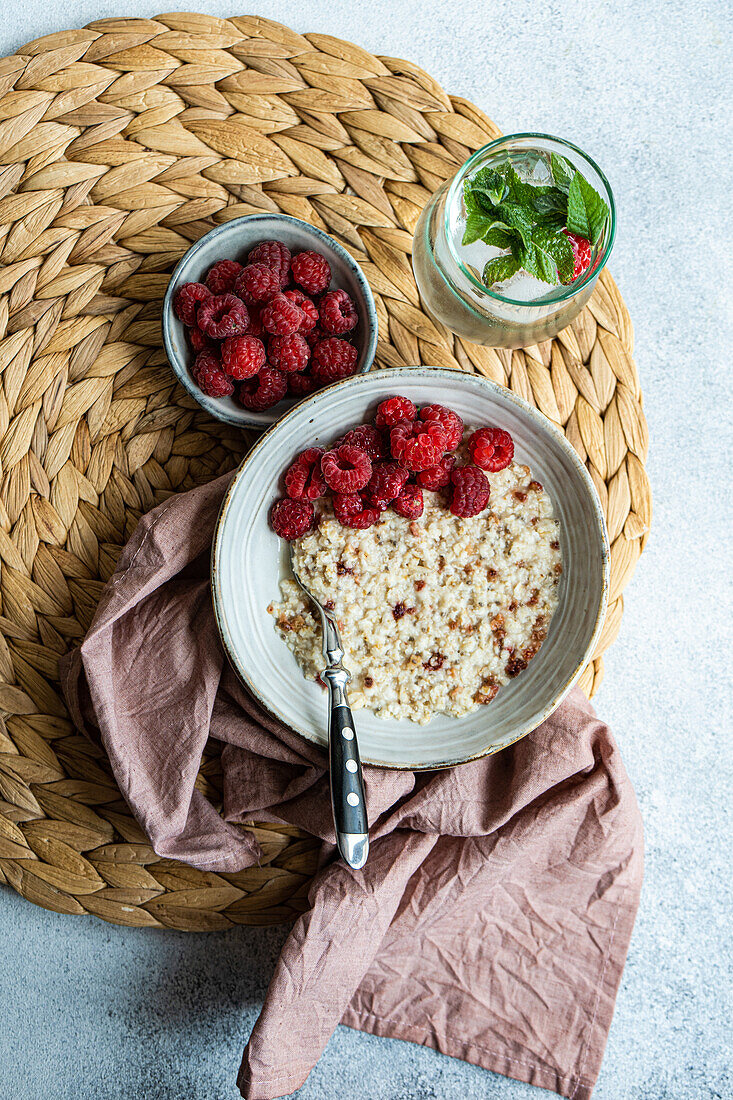 From above healthy breakfast with oatmeal with fresh organic raspberries and homemade lemonade on concrete table