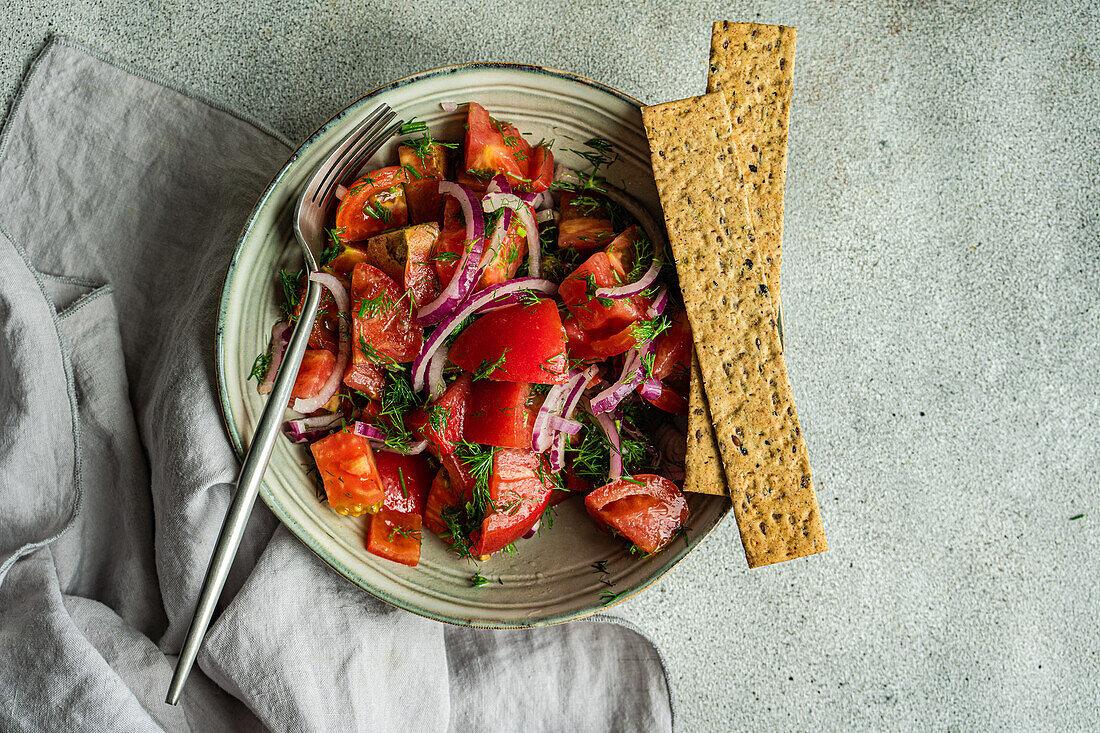 From above of bowl with salad made of tomatoes red onion and dill herb placed near on marble table