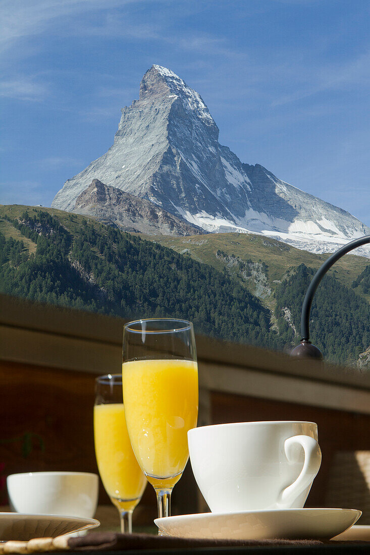 Malerischer Blick auf einen majestätischen Berggipfel mit Erfrischungen im Vordergrund auf einem Holztisch, der einen heiteren Morgen unterstreicht
