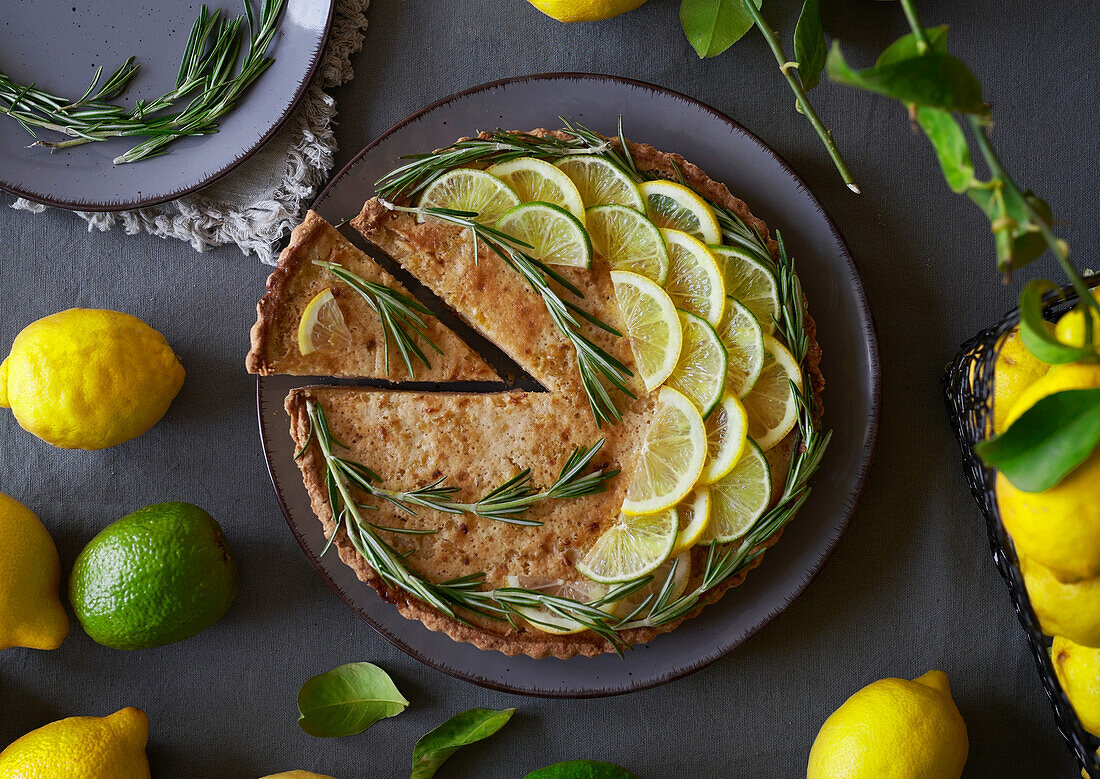 From above of round lemon pie with decorated with lemon slices and rosemary sprigs on table with a grey towel