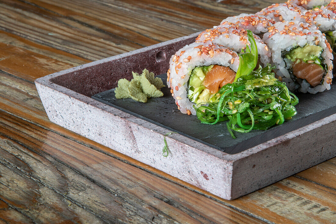 Nahaufnahme einer servierten Reihe von Avocado-Thunfisch-Uramaki-Sushi-Rollen mit Wakame-Salat auf einem Betonteller