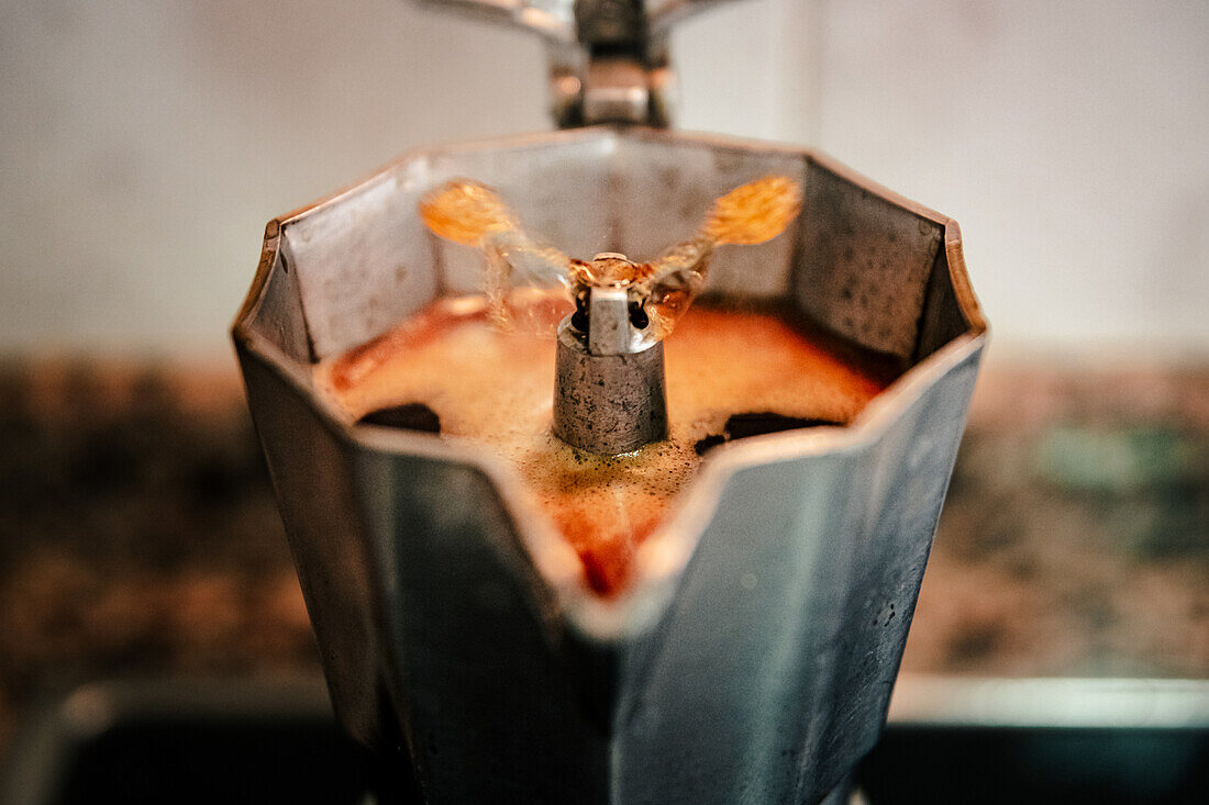 Nahaufnahme von blubberndem Kaffee in einer offenen Espressomaschine, die das reiche Aroma und die Konsistenz von frisch gebrühtem italienischen Kaffee in einer gemütlichen Umgebung einfängt