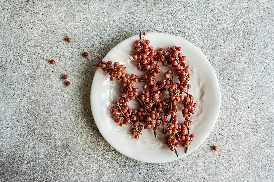 Top view of scattered organic buffaloberries on a white ceramic plate with a few berries fallen on the grey surface in soft daylight
