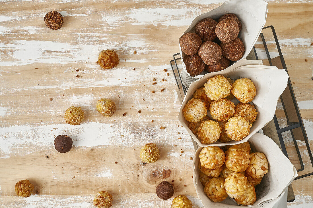 Draufsicht auf süße Panellets in Zeitungspapier-Tüten in einem schwarzen Korb auf einem braunen und weißen Holztisch