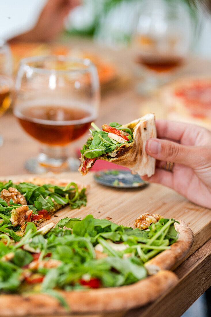 Selective focus of crop person eating appetizing pizza with cheese and lettuce on wooden table with glasses of wine