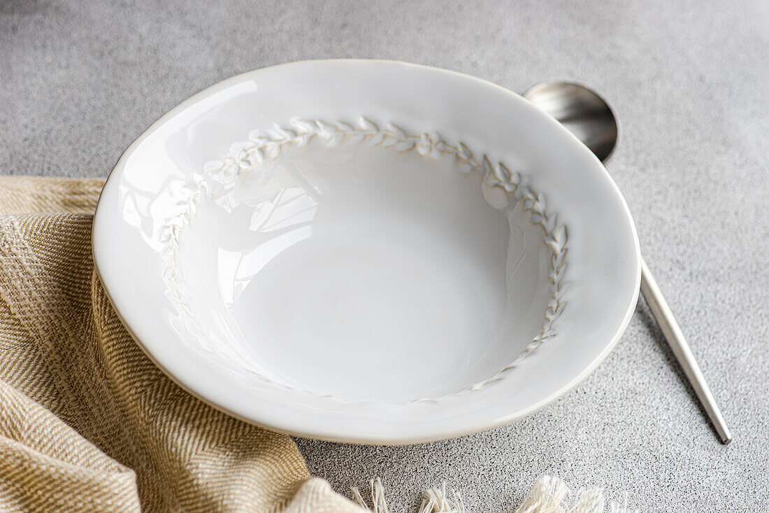Hoher Winkel eines herbstlich gedeckten Tisches mit einer weißen Keramikschale zwischen Löffel und Serviette auf einer grauen Fläche