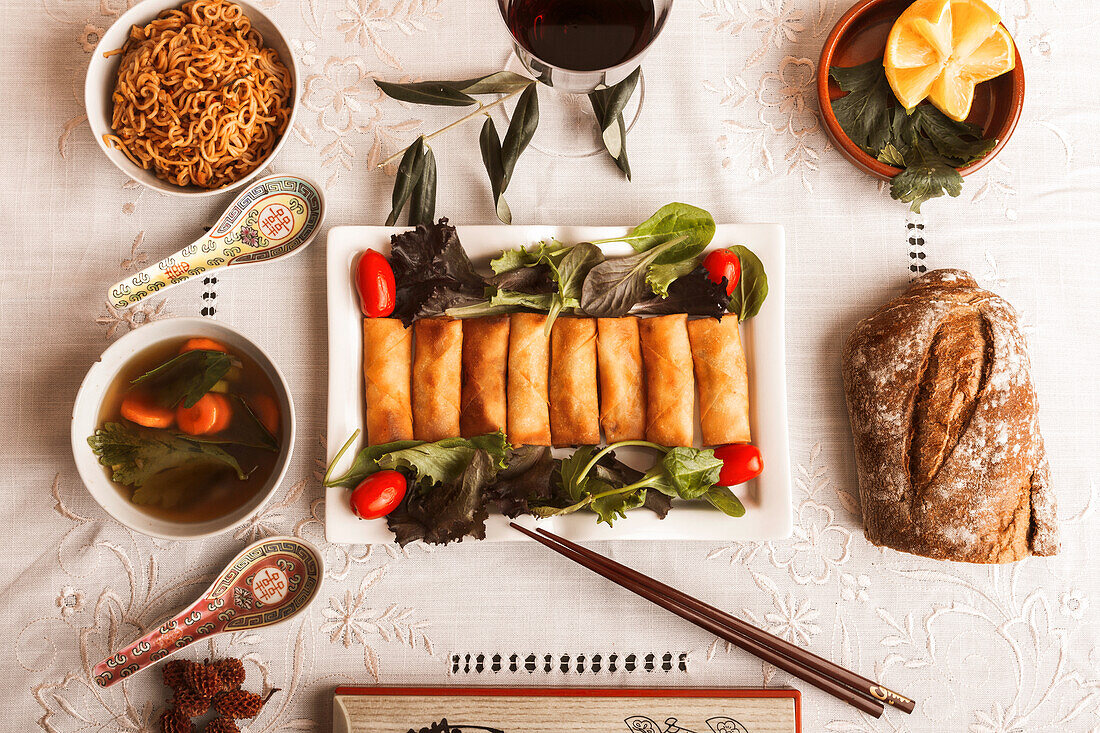 A beautifully arranged platter of vietnamese rolls with greens and sauces, accompanied by soup and bread, perfect for a gourmet meal setup.