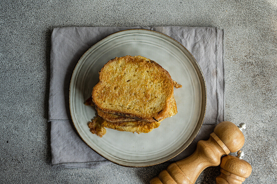 Top view of sliced of fried bread with egg coating on ceramic plate next to cloth napkin on concrete background