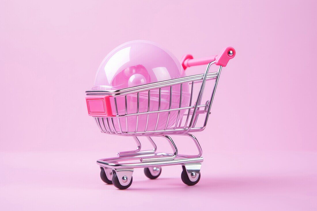 Composition of miniature shopping trolley with pink mockup ball placed on pink background