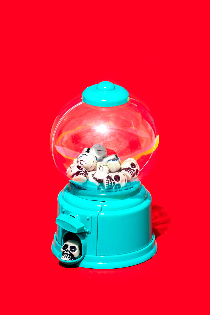 Heap of little human skulls inside transparent round vending machine isolated against vivid red backdrop
