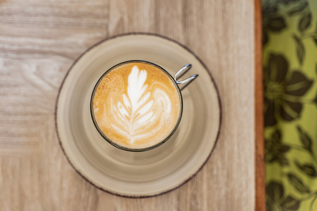 Nahaufnahme von heißem Kaffee mit kreativer Latte Art, serviert in einer Tasse mit Untertasse auf einem Holztisch im Cafe