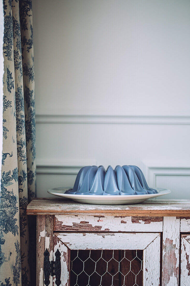 Sweet vegan blue panna cotta dessert on plate placed on vintage wooden cabinet near curtain