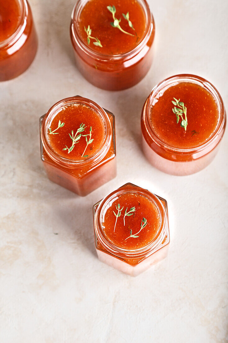 From above jars filled with homemade fruit jam placed on table with green sprigs of thyme