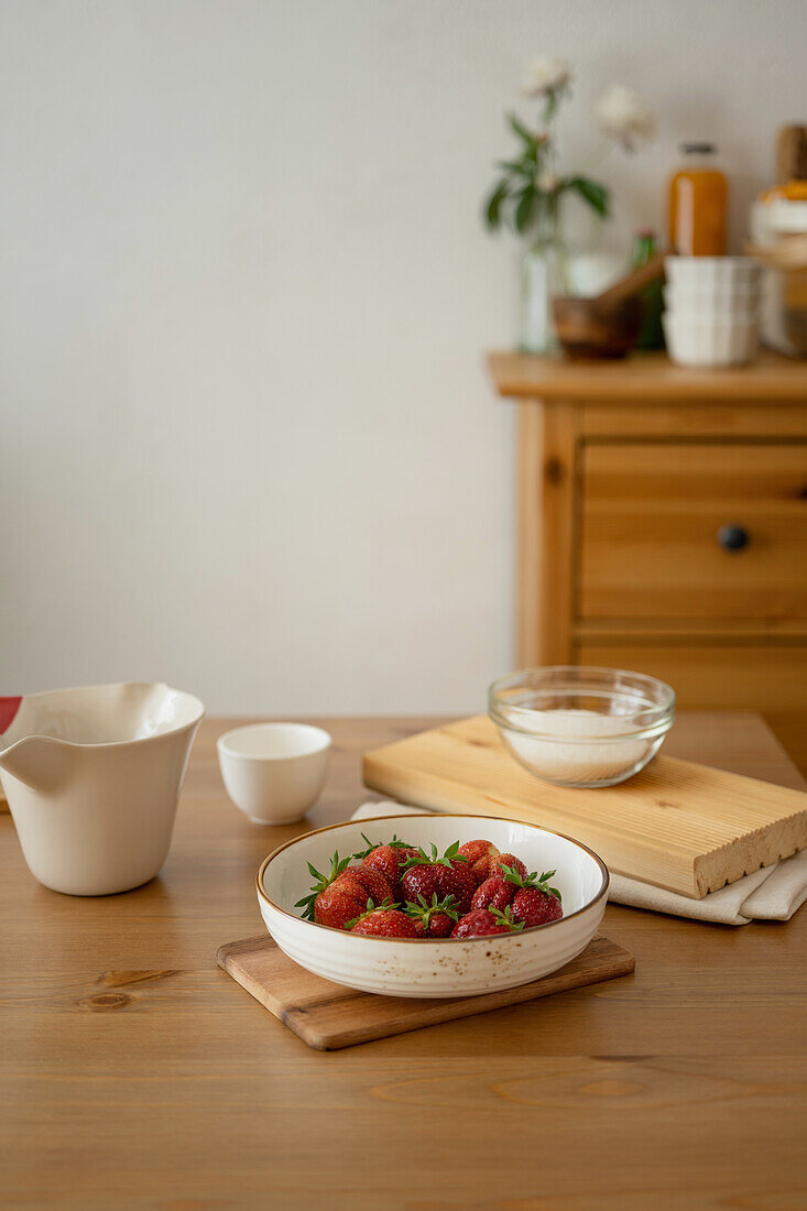 Schale mit frischen roten Erdbeeren in einer Schüssel zum Kochen auf einem Holztablett über dem Tisch während der Zubereitung von Marmelade zu Hause