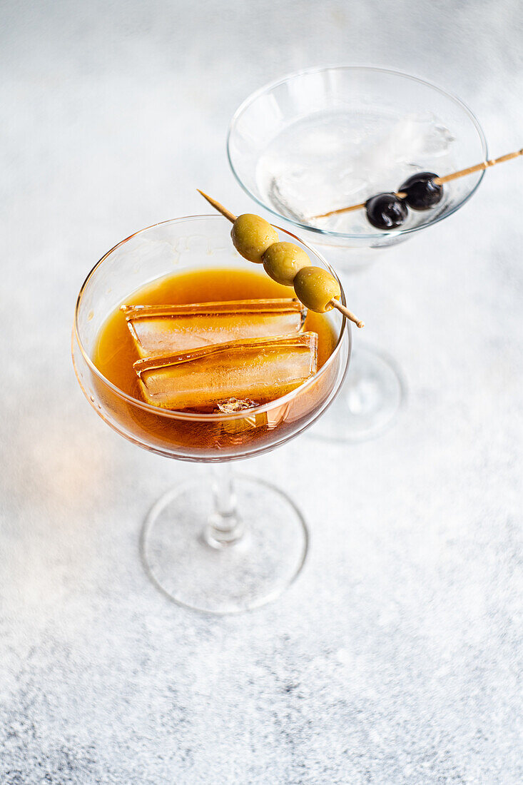 High angle of glasses of alcoholic cocktails with whiskey and sticks of oily olives slices on gray background in studio
